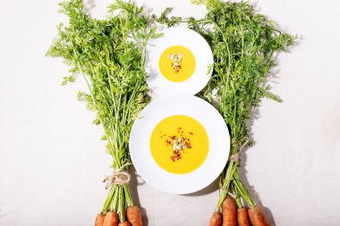 Seramik tabakta havuç püresi çorbası ve koyu dokuda taze organik havuç. Üst manzara, düz yatış. Boşluğu kopyala