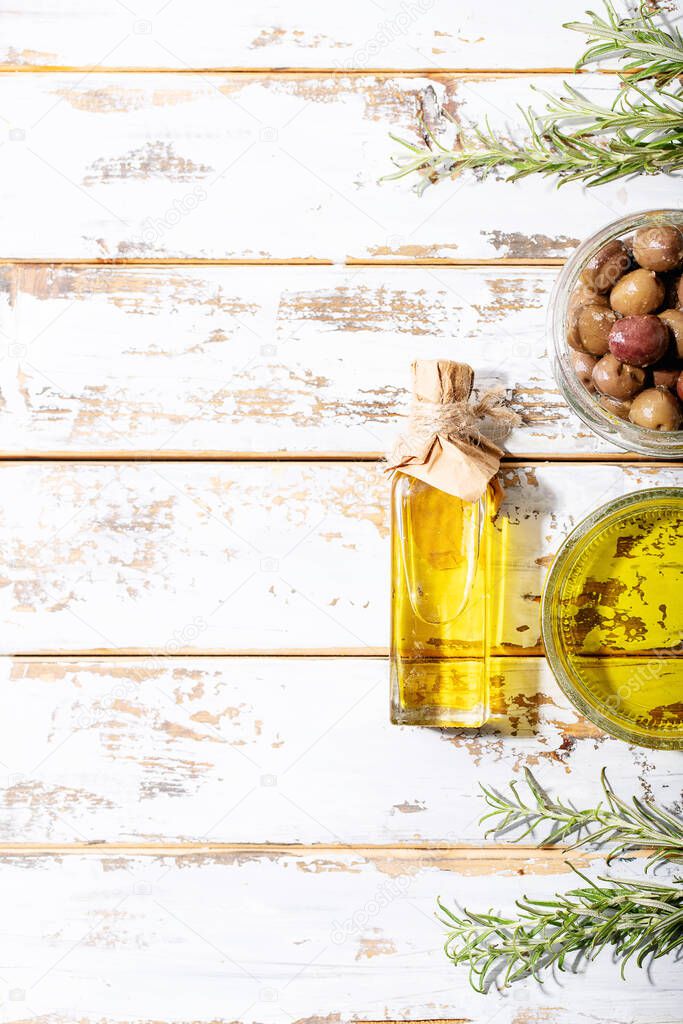 Olive oil in glass bowl served with fresh olives over white wooden background. Top view, flat lay. Copy space