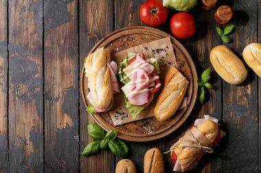 Ev yapımı sandviç: domates, peynir, jambon, marul ve Fransız ekmeği tahtanın üzerinde kahverengi ahşap arka planda.