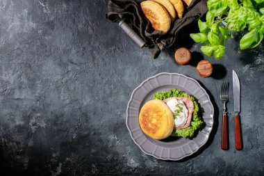 İngiliz çörekleri ve koyu dokular üzerine taze fesleğenle servis edilen pişmiş yumurtalı Benedict. Boşlukları kopyala