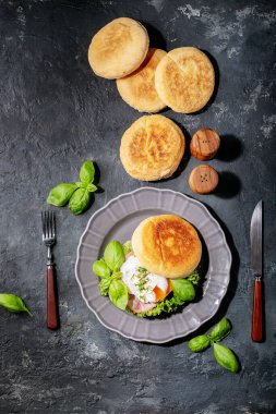 İngiliz çörekleri ve koyu dokular üzerine taze fesleğenle servis edilen pişmiş yumurtalı Benedict. Boşlukları kopyala