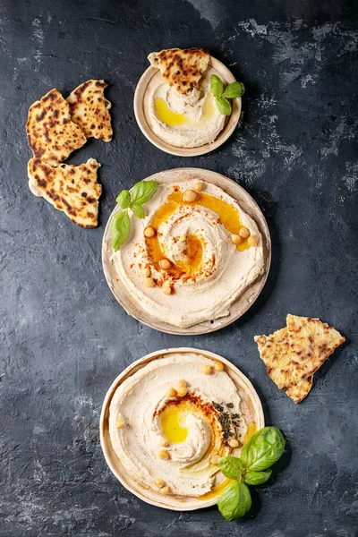 Hummus with olive oil and ground cumin in ceramic plate served with homemade pita bread over dark texture background. Top view, flat lay