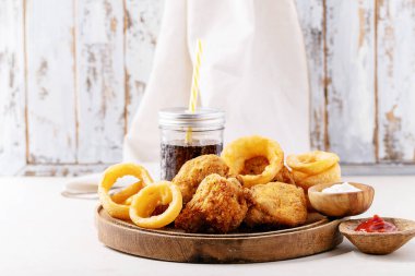 Kızarmış kızarmış tavuk filetosu, kızarmış soğan halkaları ve patates yanında kola ve sosla servis ediliyor.