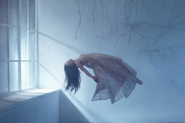 Девушка-призрак с длинными волосами в винтажном платье. Фотография левитации, напоминающая сон. Тёмная готическая комната с ветвями и огромным окном затопленного света. Спящая красавица
