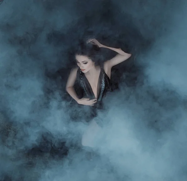 黑暗的吸血鬼女王躺在她的黑色礼服上的雾拥抱与深领口 女孩被烟雾笼罩着 就像毯子上的云彩 哥特式气氛 睡美人 — 图库照片