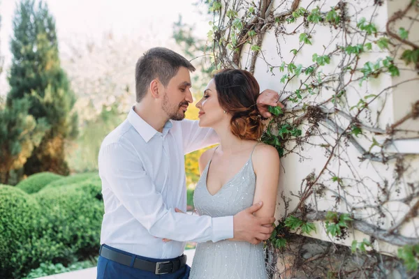 A loving couple hugs in a blooming garden. Red-haired girl in a modest, gray dress in rustic style. Stylish and discreet wedding day. A neat, collected hairdo in an airy beam. Art photo.