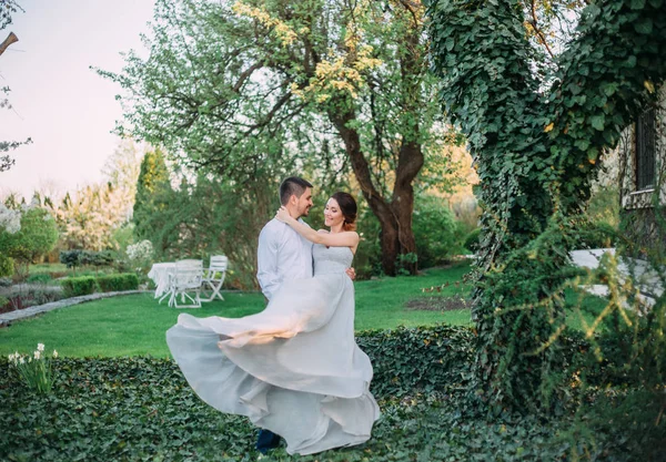 The husband is circling his favorite woman in the arms. Red-haired girl in a modest, gray dress in rustic style. Stylish and discreet wedding day. A neat, collected hairdo in an airy beam. Art photo.