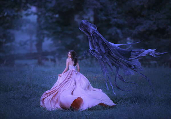 Beautiful girl in a long, pink, fluttering dress runs away from death in the form of a dark demon who came out of hell. Frightened brunette girl looks around. Artistic, gothic photo in cold colors.
