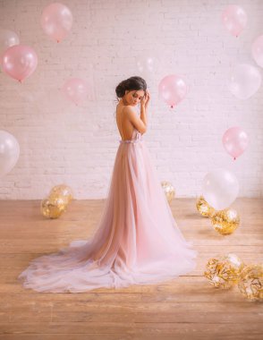 İhale fotoğraf içinde a muhteşem pembe mor elbise uzun bir tren ile giyinmiş bir inanılmaz temiz saç modeli, siyah saçlı bir kızla. şirin tutuşup, arka plan beyaz ve pembe top.