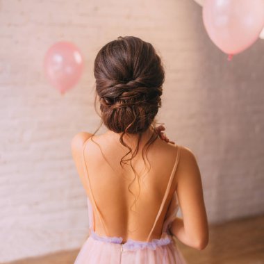 a young attractive lady, a peach dress with a purple color, shows a bare open back and a great neat dark hair hairstyle, standing in a bright spacious room with pink balls, no face in the photo. clipart