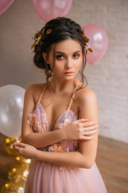 siyah saçlı ve bir altın RIM ile gizemli bir genç bayan inanılmaz kahverengi gözleriyle kameraya bakarak, hafifçe omzuna elini dokunmadan, balonlar yakınındaki hafif bir şirin elbise.