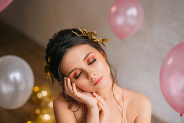 miniature girl with innocent childish face, tender skin and dark hair closed her lovely eyes and naps. Cute and touching photo with balloons and a garland. princess in peach with purple light dress.