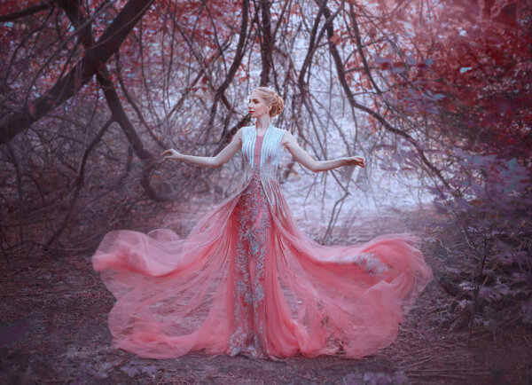 Attractive girl with gorgeous blond hairdo in the forest near the branches of trees, dressed in a light amazing pink tender dress, throws it down, flying fluttering clothes, art photo, creative color.