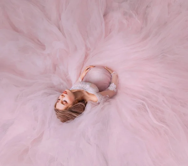 Εξαιρετικό ελκυστική αθώα κοπέλα έγκυος ΕΣΔ στο πάτωμα στο μαύρο του ένα ακριβό πανέμορφο κομψό ροζ φόρεμα, τα γυμνά τους ώμους, έκλεισε τα μάτια της στα όνειρα και αγκαλιάζει απαλά το μωρό στην κοιλιά — Φωτογραφία Αρχείου