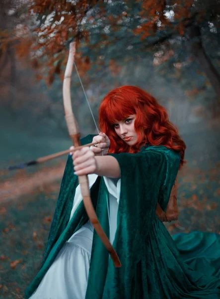Kızıl saçlı kız bir yay onun elinde tutan bir ok yönetmenlik, savaş, savaşçı görüntü zümrüt pelerin içinde elfin ve beyaz elbise, sanat soğuk renkler, Gotik sis deneyimli avcı gider — Stok fotoğraf