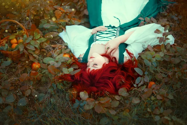 Underbara rödhåriga prinsessan liggande på marken, slits med blad, försiktigt lade sin hand på hennes bröst, klädd i en lång grön och vit latte, sidentyg, äpplen föll ur korgen, modig flicka — Stockfoto