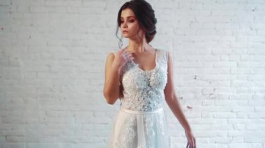 nazik bir saç modeli koyu saçlı tatlı bayan uzun zarif beyaz elbiseli, stüdyoda ayakta poz, elini boyun için yükselterek, bu güzel yüzün tarafa beyaz studio dönüm