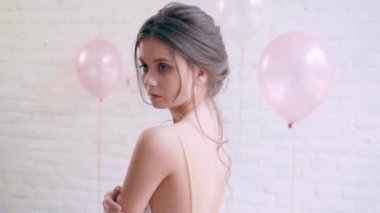 çocukça bir yüz ile sevimli sevimli kız poz, bir modeli ideal bir ihale cilt ile açık bir çıplak sırt ile ücretsiz ışığı elbiseyle duruyor ve incelikle geri dönüş göğsüne ellerini koyar