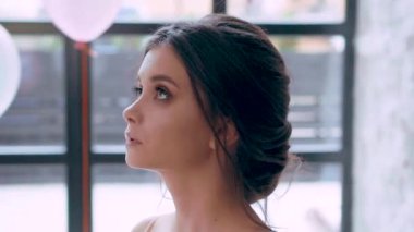 Çocukça yüz ve mükemmel sağlıklı cilt, yumuşak özellikleri, çekici çekici esmer örnek alıyor, gözleri düşürür, yavaşça boyun ve göğüs, büyük pencere ve beyaz balon yakınındaki üzerinden elini çalışır