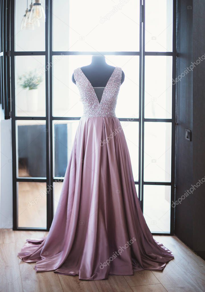 beautiful monophonic satin silk pink purple purple long cute dress with a deep neckline for the princess, put on a mannequin, decorated with big sequins and rhinestones. perfect tailoring