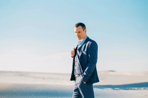 Serious adult handsome man in a blue strict suit and heavenly shirt on the wedding day, the image of a man thinking, a stylish businessman in the sand desert alone, an amazing guy in stop moment — Stock Photo, Image