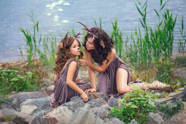 Anne ve çocuk aile fotoğrafı, fakat büyük bir göl kıyısında taşları, masal karakterleri üzerine oturuyorsun, Bebek ilgiyle ararken annesi kızı için uzanıyor