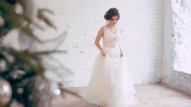 beyaz uzun elbise yavaşça adımları loft tarzı oda, yastıklar, yılbaşı ağacı, Gelin pozlar, spin, geniş pencere içinde hafif ahşap zemin üzerinde gizemli bir şekilde görünüyor kameraya harika inanılmaz kadın