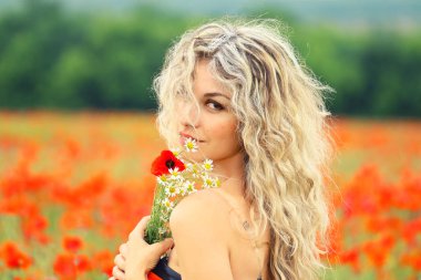 hafifçe gülümseyerek, bir avuç çıplak omuz yakınındaki kır çiçekleri tutarak oldukça çekici kadın sarışın kıvırcık saçlı güzel bir kırmızı haşhaş alan yüzüne düştü, fotoğraf makinesinin için