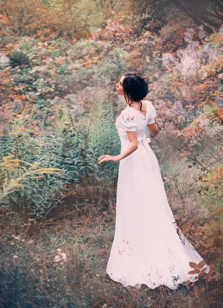 Deliziosa principessa in un lungo abito bianco si è persa in una foresta lontana, ascolta il rumore e il canto degli uccelli, si ferma in attesa, una fiaba in un lungo abito bianco vintage di seta elegante — Foto Stock