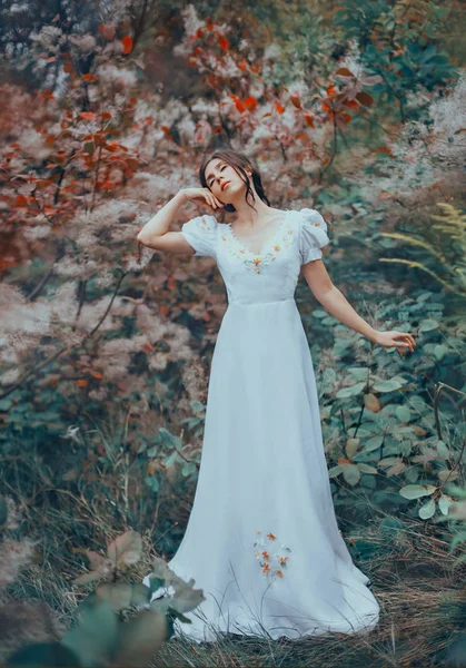 Μυστηριώδης κυρία μόνη στο πολύχρωμο παραμυθένιο δάσος, Χορεύοντας με τα μάτια της κλειστά, αυξάνοντας το χέρι του στο μάγουλό της, μελαχρινός νεράιδα σε ένα μακρύ άσπρο vintage φόρεμα σε floral μοτίβα, μπούκλες πέφτουν στο πρόσωπό της — Φωτογραφία Αρχείου
