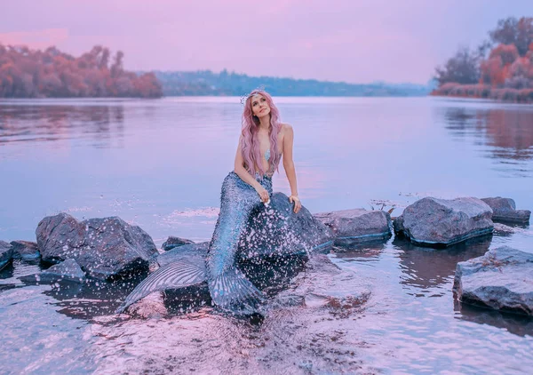 童话般的海皇后, 粉红色的长发, 水母坐在石头上, 梦幻般地看着紫色的天空, 美人鱼飞溅, 洒上长长的、有鳞片的尾巴的水, 柔和的色彩, 海洋领主的女儿 — 图库照片