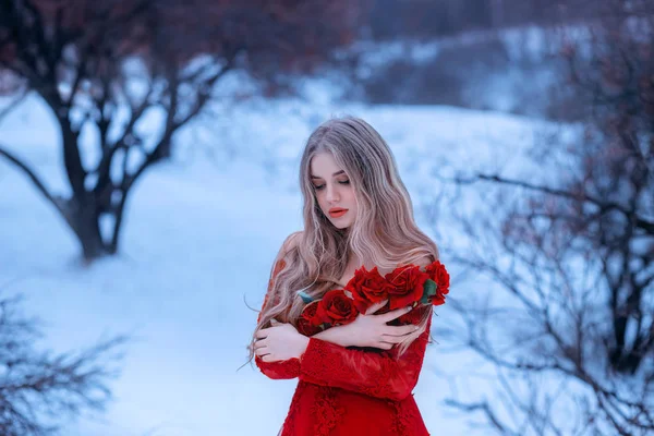 Magical image of attractive blonde girl in gorgeous red dress decorated with flowers, Rose princess trying to keep warm in snowy forest, wonderful work of make-up by visagiste and photographer — Stock fotografie