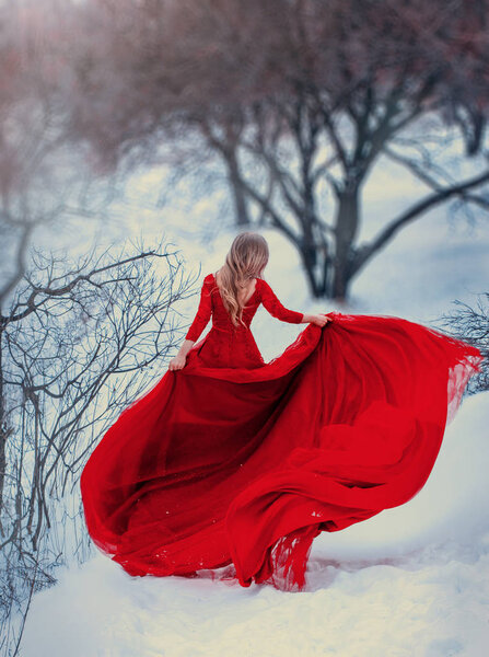 Mysterious girl runs, spinning in a red dress, with a very long train. Hair is flying in the wind. Photo without a face, from the back. Woman escapes from problems, gaining freedom. Background winter.