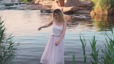 pozitif sarışın kız çıplak ayakla parlak bir sıcak gün parlama su güneş gibi muhteşem bir deniz kızı, onun pembe kadar nazik hippi elbise sinekler ve flutters, nehir kenarında bir taşa dans