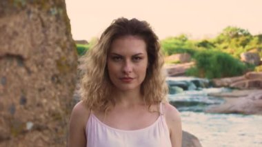 Makyaj, doğal kadın güzelliğinin, olmadan sarışın kıvırcık saçlı çekici kız nehir kıyısında yüksek rock, tutkulu ve oynak bak kahverengi koyu renk gözleri bir taş yakın çekim portre çekici