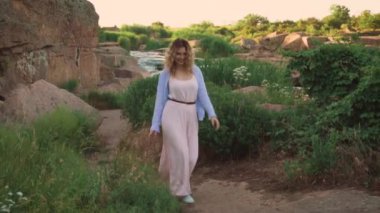 sarışın saç kesiminden rezerv, güneşli yeşil yol boyunca keyifli zarif kız şarkı küçük bir dans, bir pembe uzun yaz elbise ve eğleniyor, olumlu gülümseyen mavi gömlek giymiş