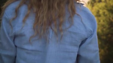 yumuşak sulu çiçekler ile parlak bir olumlu video, büyüleyici bir zarif kız ileri bir ışık yaz şeftali elbise ve mavi bir gevşek gömlek giymiş güneşe, eğlence için yüzü olmayan yürüme gider