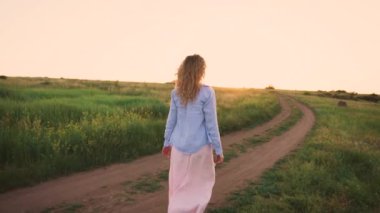 muhteşem manzara, yeşil alan, parlak ışık gökyüzü, ince sarışın saç kesiminden uzun gevşek pembe hassas basit elbise ve mavi gömlek, yol boyunca kızla tutan küçük daisy onun elinde, yüzü olmayan