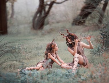 Anne ve kızı, çocuk ve anne için yaratıcı fotoğraf fikir giyinmiş geyik ormandaki çimenlerin üzerinde oynarken flüt, melodi dikkatle takip kız, sanat bir kadın oturuyor gibi işleme