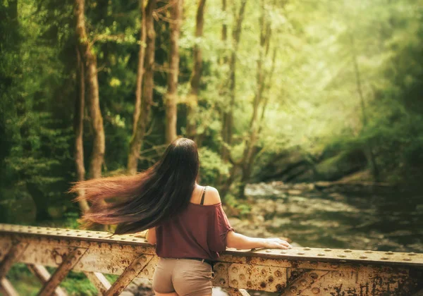 Magnifica foto in movimento, sottile ragazza attraente agitando volare capelli chiari scuri, si erge su un ponte su un fiume freddo trasparente in Georgia, affascinante splendida natura è luminoso e succoso — Foto Stock