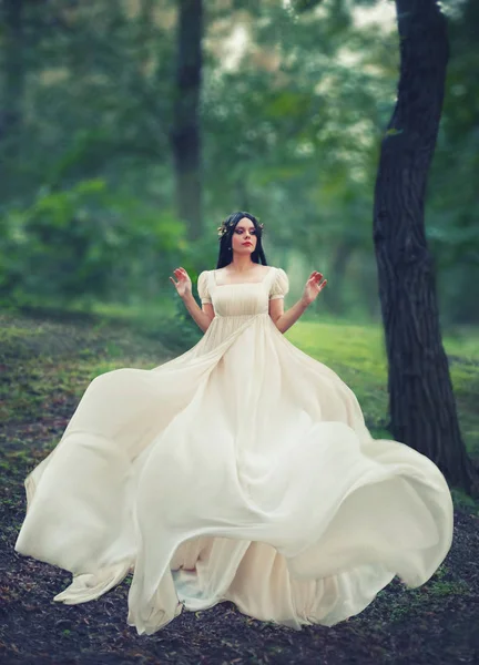 Encantadora princesa en un bosque verde brillante baila solo, chica de pelo oscuro en vestido largo blanco elegante suave con tren de vuelo aleteo, dobladillo, corona de oro, historia de Blancanieves, hada de las flores — Foto de Stock