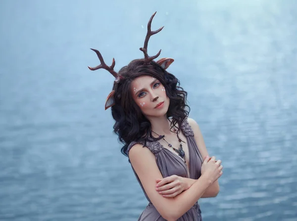 Interesante foto de la madre ciervo en frente del lago lagle, personajes del bosque de hadas, imagen de una mujer-faun triste cerca de un gran lago, maquillaje inusual, con cuernos caseros y orejas en el pelo rizado oscuro — Foto de Stock