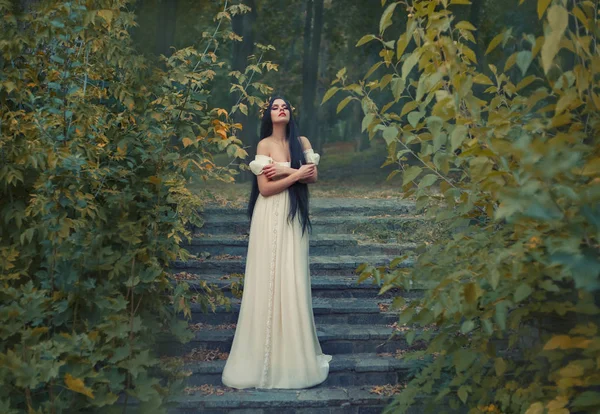 En prinsessa med sexuellt bara axlar har ett ögonblick av tystnad och ensamhet. Svart långt hår, gyllene krans, cream silk vintage klänning. Runaway Bride — Stockfoto