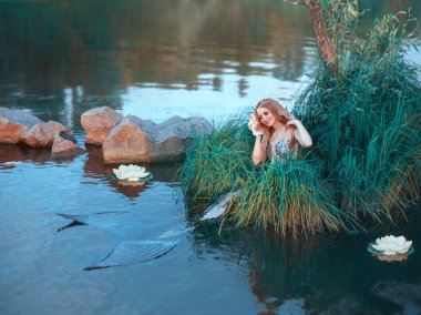 parlak yeşil çim sıcak bir nehir kıyısında şirin deniz kızlık oturan, gülümseyen ve kabuk, sarı saçları ile efsanevi bir deniz kızı ve bir nehir diadem başında arkadaşları ile sohbet