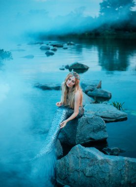 harika bir deniz kızı yavaşça ve sorunsuz taş göle, oturur gibi sarışın kız pullu kuyruğunu elini tutan, onu deniz diadem koymak suya indirdi fin bakar