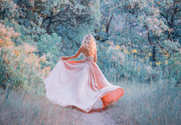 Young slim shapely girl with long blond curly hair wearing a elegant satin flapping silk pink dress with a lace top, spinning and running in the autumn orange forest. no face. art photo background.