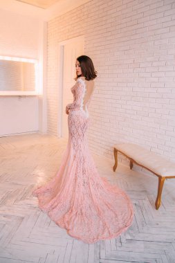 Açık bir sırt ile pahalı, pembe elbiseli bir poz lüks esmer kız, bob saç kesimi ile. Beyaz Oda, Prenses. İskandinav minimalist tarzı iç. Balo ve parti için görüntü