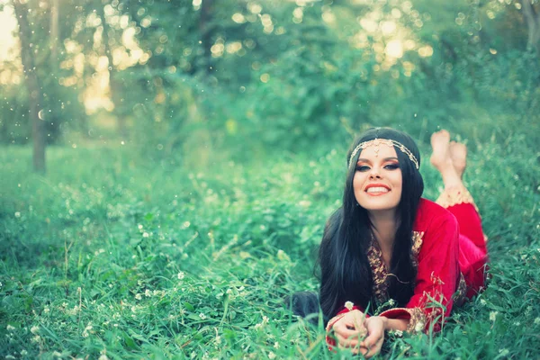 Gelukkig aantrekkelijke vrolijke vrouw met lange zwarte haren liggen op de vroege gras, felle zon en schittering, met brede glimlach rusten in de weide, verstandig genezer verzamelt geneeskrachtige kruiden, vrije tekst ruimte — Stockfoto