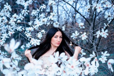 hoş genç bir siyah saçlı mavi gözlü Bayan çiçek açan Manolya bahçede duruyor. saç kadar elleri ile inanılmaz fotoğraf Beyaz filtre, sanat fotoğraf işleme soğuk tonlarında uçar
