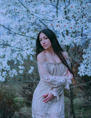 Açık omuz ile keyifli bir vintage elbise giydirme sevimli çekici Bayan siyah uzun saçlı ve yeşil gözlü, çiçek açan Manolya duran ile serin sanat fotoğraf işleme